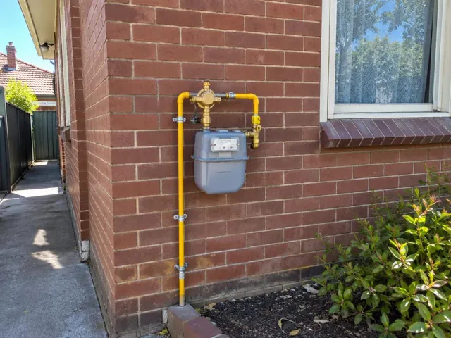 Outdoor gas meter and yellow pipework on a brick house wall beside a window in Fairfield