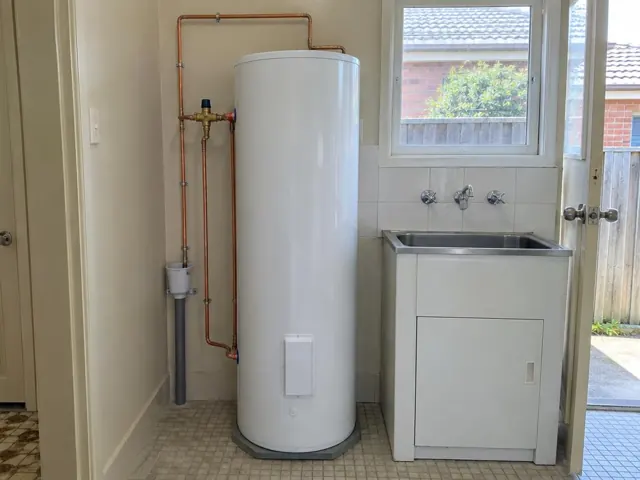 White hot water cylinder beside a laundry sink with copper pipework and tiled walls in Merrylands