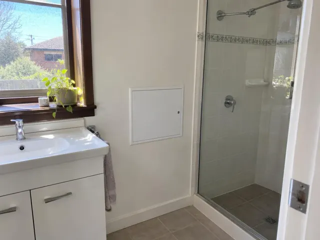 Bathroom wall with a small access panel beside a vanity and tiled shower in Merrylands
